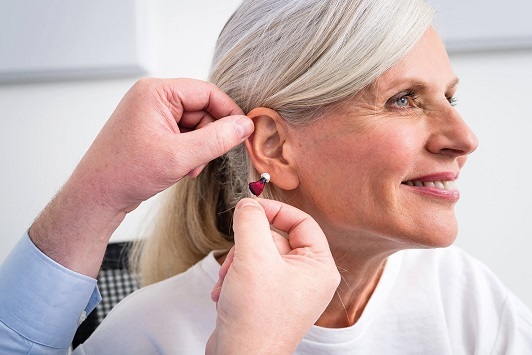 Eine ältere Frau bekommt ein Hörgerät eingesetzt, Hörakustiker passt Hörhilfe an.